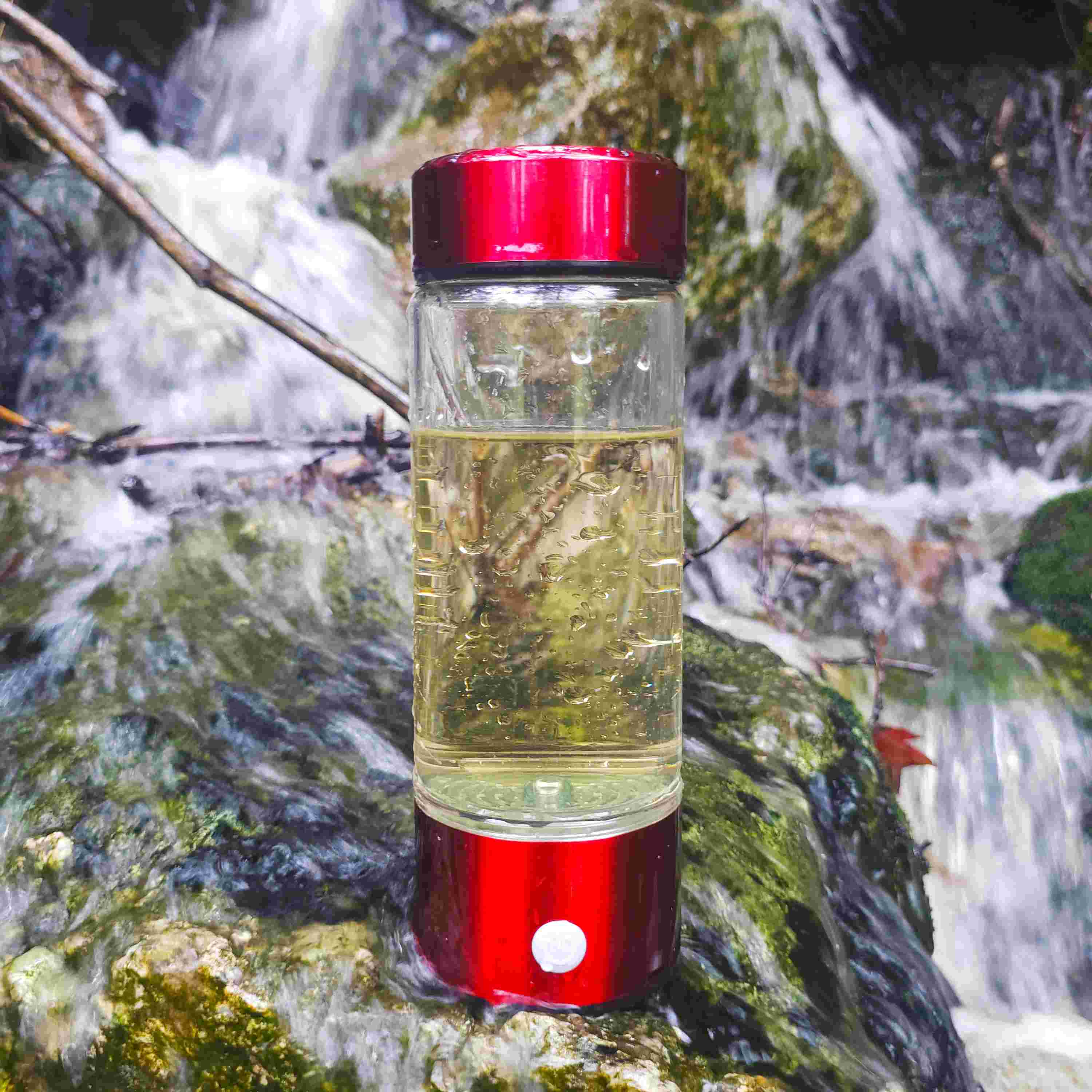 Red hydrogen water bottle placed in front of waterfall outdoors