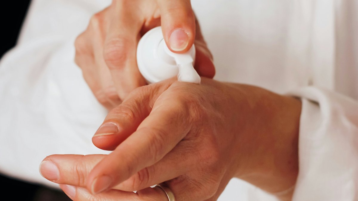 Hands applying pain relief cream from a pump bottle, the way Aspercreme's lidocaine cream is meant to be used