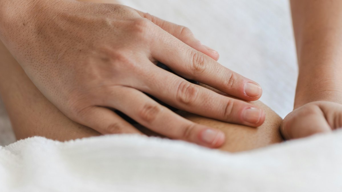 Hand massaging a person's leg muscle over a white towel, the kind of muscle soreness Tiger Balm is meant to relieve